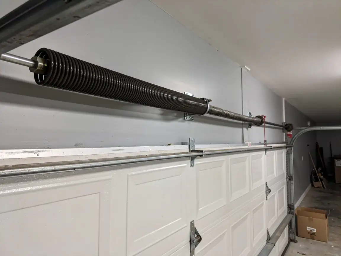 A garage door torsion spring is mounted above a white garage door.